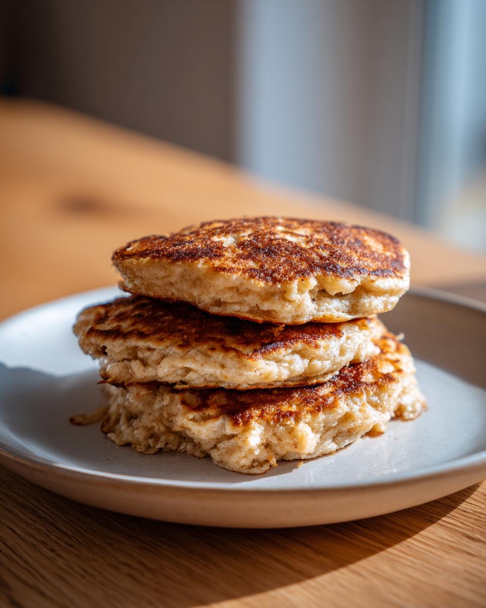 A stack of three fluffy banana oatmeal pancakes with golden-brown, slightly crispy edges, served on a light plate.