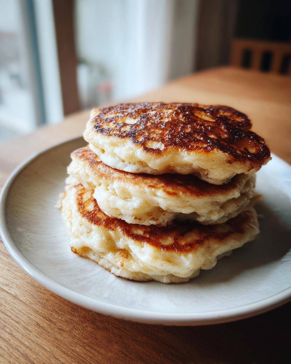 A stack of three fluffy banana oatmeal pancakes with golden brown edges served on a light plate.