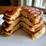 Close-up of a stack of fluffy coconut flour pancakes cut in half to show the interior texture, drizzled with syrup.