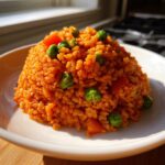 A perfectly molded mound of fluffy, orange-red Spanish rice mixed with bright green peas and diced carrots.