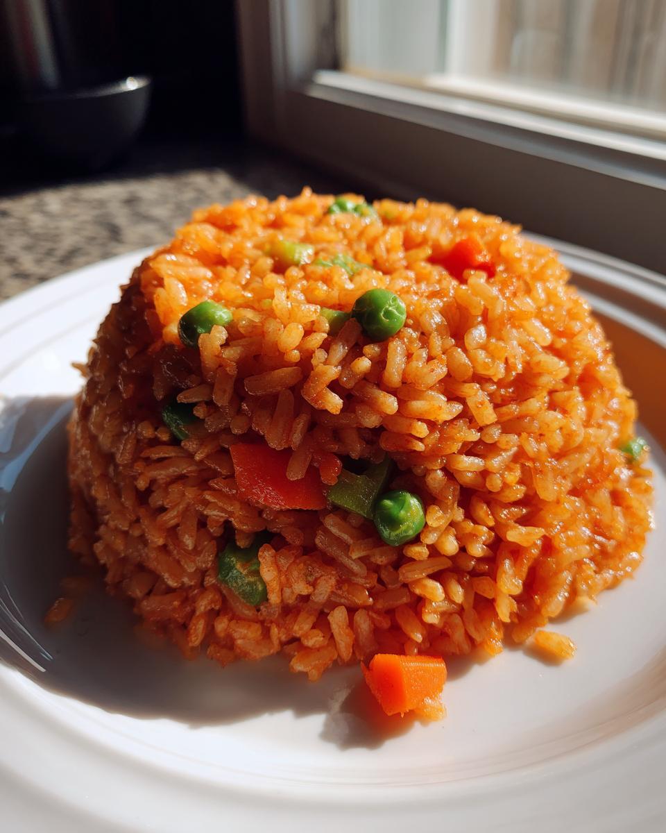 A mound of fluffy, orange-colored Spanish rice mixed with bright green peas and diced carrots on a white plate.
