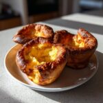 Three perfectly risen, golden brown yorkshire pudding resting on a light-colored plate.