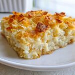 Close-up of a square serving of creamy funeral potatoes recipe with a golden, crispy topping.