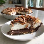 A thick slice of german chocolate pie featuring a chocolate layer, whipped topping, and toasted pecans and coconut.