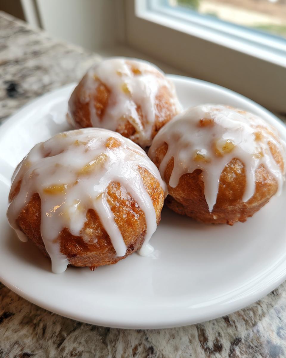 Three golden brown baked apple fritters generously drizzled with a thick white glaze, served on a white plate.