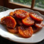 A plate piled high with glistening, round slices of candied sweet potatoes coated in a rich, brown sugar glaze.