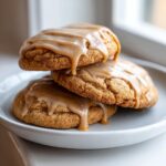 Three delicious maple cookies stacked on a light gray plate, drizzled heavily with a thick, glossy maple glaze.