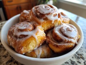 Close-up of several gooey cinnamon roll bites topped with white icing, piled high in a white bowl.