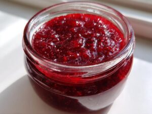 Close-up of bright, glistening homemade raspberry jam filling a small glass jar.
