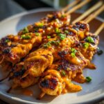Close-up of grilled bang bang chicken skewers generously drizzled with spicy orange sauce and topped with chopped green onions.