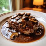 Close-up of a perfectly cooked Salisbury steak smothered in brown mushroom gravy.