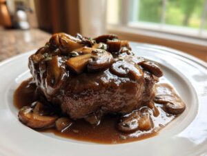 A close-up of a juicy Salisbury steak smothered in rich brown mushroom gravy and garnished with fresh thyme.