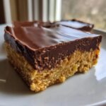 A close-up of a rich, two-layered lunch lady peanut butter bars slice with a thick chocolate topping.