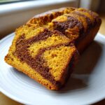 Two slices of marbled pumpkin sourdough loaf showing vibrant orange and dark brown swirls on a white plate.