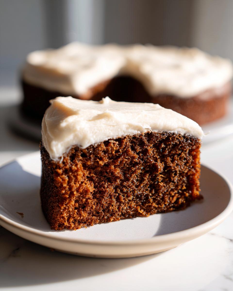 Close-up of a rich, dark slice of applesauce cake topped with thick white frosting on a small plate.