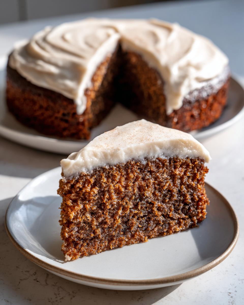 A close-up slice of dark, moist applesauce cake topped with thick cream cheese frosting and a sprinkle of cinnamon.
