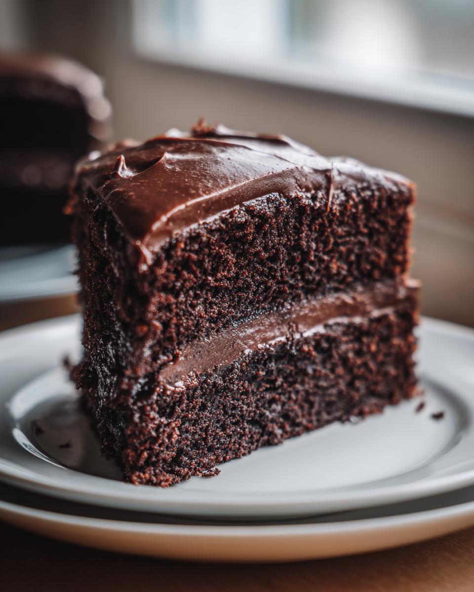 A close-up of a moist slice of rich chocolate fudge cake with thick fudge frosting.