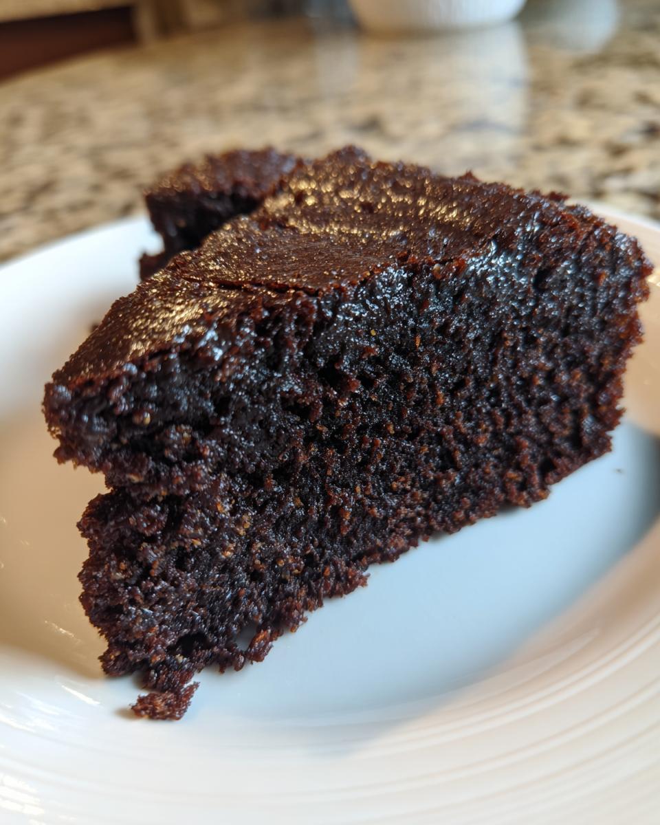 Close-up of a rich, dark, and moist slice of date brownies served on a white plate.