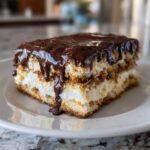 A decadent slice of chocolate eclair cake featuring layers of cream and graham crackers topped with dripping chocolate glaze.