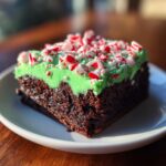 A single square of rich chocolate peppermint brownies topped with bright green frosting and crushed candy canes.