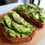 Two slices of toasted bread topped with mashed and sliced avocado, seasoned with salt and pepper for delicious avocado toast.