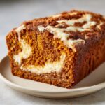Close-up of a freshly baked pumpkin cream cheese bread loaf showing the moist orange crumb and cream cheese swirl.