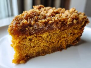 Close-up of a moist slice of pumpkin crunch cake showing the orange cake base and thick, brown, crunchy topping.