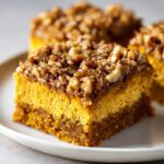 A square slice of rich, layered pumpkin crunch cake topped with crunchy pecans and streusel.