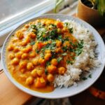 A plate featuring creamy pumpkin curry loaded with chickpeas next to fluffy white rice, topped with fresh cilantro.
