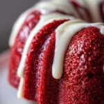 Close-up of a vibrant red velvet bundt cake drizzled generously with white cream cheese frosting.