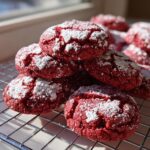 A stack of bright red velvet cake mix cookies dusted heavily with white powdered sugar, resting on a cooling rack.