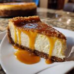 A close-up of a slice of creamy salted caramel cheesecake dripping with thick caramel sauce on a white plate.