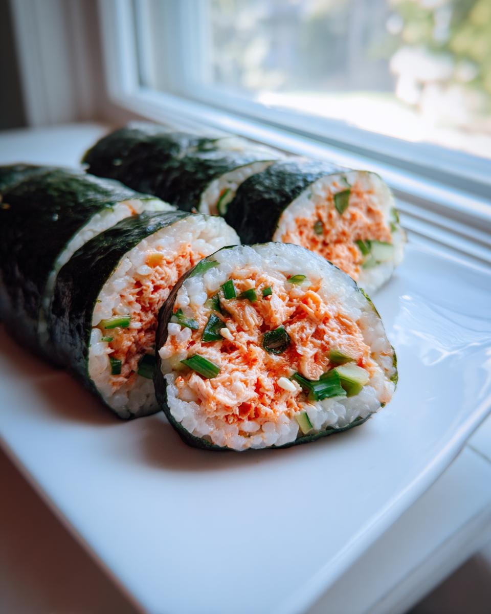 Close-up of sliced tuna kimbap rolls showing the filling of spicy tuna, rice, and green onions, set against a bright window.