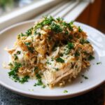 A close-up of shredded slow cooker garlic parmesan chicken coated in a creamy sauce and topped with fresh parsley.