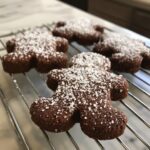 Close-up of several soft gingerbread cookies shaped like gingerbread men, dusted with powdered sugar, cooling on a wire rack.