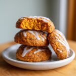 A stack of three soft, orange persimmon cookies drizzled with white icing, one cookie has a bite taken out.