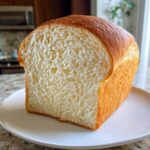 A freshly baked loaf of sourdough sandwich bread, showing a soft, even crumb structure and golden crust.
