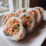 Five slices of homemade tuna kimbap filled with spicy tuna mixture and topped with green onions, served on a white plate.