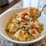 A spoonful lifted from a bowl shows tender shredded chicken and a fluffy dumpling from the amazing chicken and dumplings recipe.