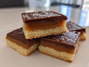 Close-up of stacked homemade Twix bars showing shortbread, thick caramel, and chocolate topping sprinkled with sugar.
