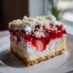 Close-up of a decadent slice of strawberry shortcake cheesecake showing layers of crust, cream cheese, strawberries, and crumble.