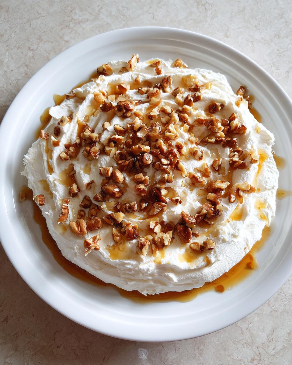 A mound of fluffy whipped goat cheese topped with chopped nuts and drizzled with honey.