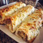 Three rolled white chicken enchiladas covered in melted, bubbly white cheese and sprinkled with herbs.