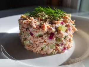 A molded serving of creamy salmon salad mixed with red onion and celery, topped with fresh dill.