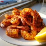 A pile of perfectly cooked, seasoned air fryer frozen shrimp served with a bright lemon wedge on a white plate.