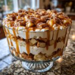 A towering caramel apple trifle layered with cream, cake pieces, apples, and drizzled generously with caramel sauce.