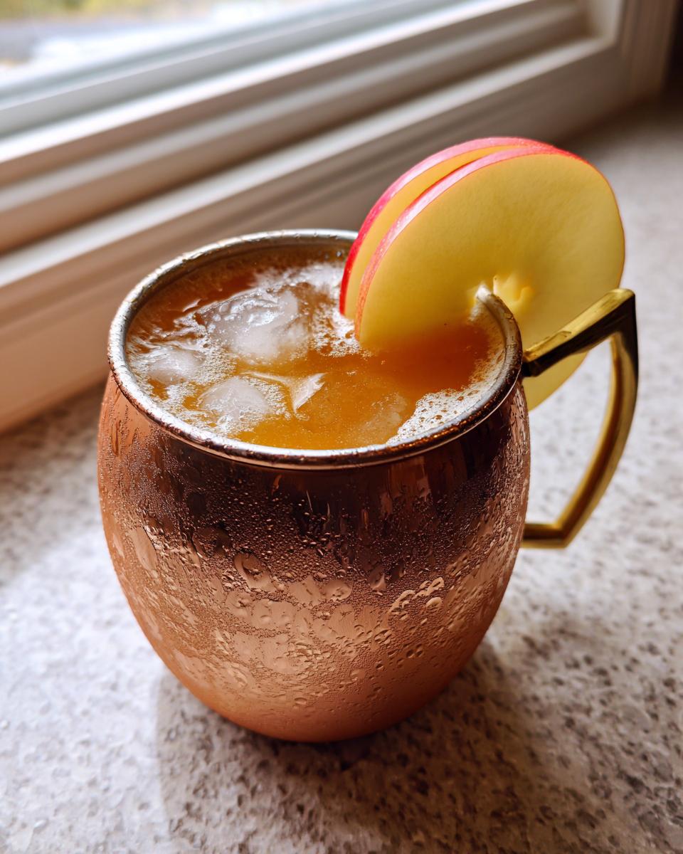 Close-up of a frosty copper mug filled with an apple cider moscow mule, garnished with thin apple slices.