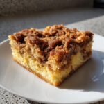 A close-up of a square slice of baked french toast with a thick, crumbly cinnamon streusel topping on a white plate.