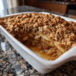 A close-up view of a freshly baked apple crisp with a thick, golden brown oat topping and bubbling fruit filling.