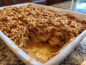 Close-up of a freshly baked apple crisp with a thick, golden brown oat topping and bubbling fruit filling.